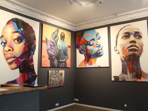 Foto einer Wand in der SOUL OF AFRIKA Galerie in München. Darauf zu sehen sind Bilder von Sarah Danes Jarrett und von Khaya Sineyile