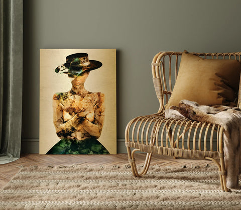 Raum mit Holzmöbeln und einem Teppich. Am Boden steht das Werk "Acacia Invert" von Linnea Frank. Es ist ein Fotodruck auf einer Gold-Dibond Metall Platte und zeigt eine Frau die ein Kleid und einen Hut trägt. Sie hat die Arme vor sich überkreuzt und legt ihre Hände in der Nähe ihrer Schultern ab. Sie sieht ruhig und mysteriös aus. Das Bild ist in den Farben Gold und Grün gedruckt.