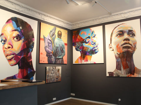 Foto einer Wand in der SOUL OF AFRIKA Galerie in München. Darauf zu sehen sind Bilder von Sarah Danes Jarrett und von Khaya Sineyile 