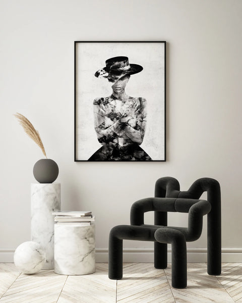 Raum mit Marmor Möbeln und einem Stuhl. An der Wand hängt das Werk "Acacia Invert"  von Linnea Frank. Es ist ein Fotodruck auf einer Metall Platte und zeigt eine Frau die ein Kleid und einen Hut trägt. Sie hat die Arme vor sich überkreuzt und legt ihre Hände in der Nähe ihrer Schultern ab. Sie sieht ruhig und mysteriös aus. Das Bild ist in schwarz-weiß gedruckt.